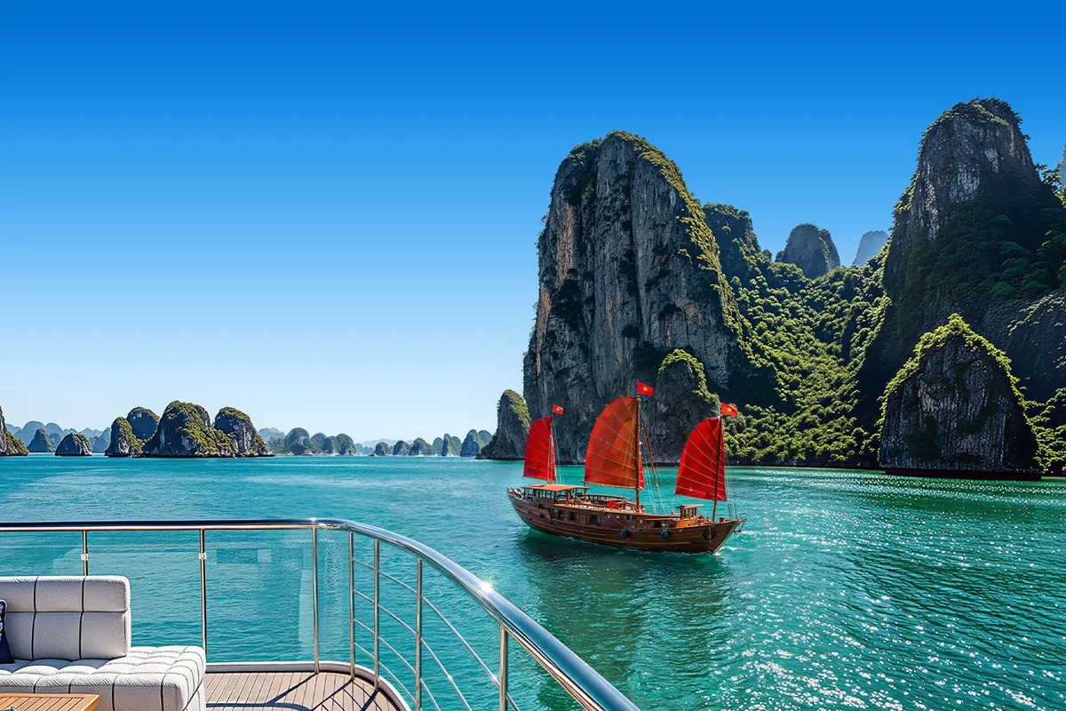 Perahu layar merah tradisional di antara tebing karst Teluk Ha Long, Vietnam.